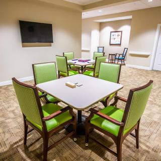 A brightly lit dining or meeting area with green chairs and a television.