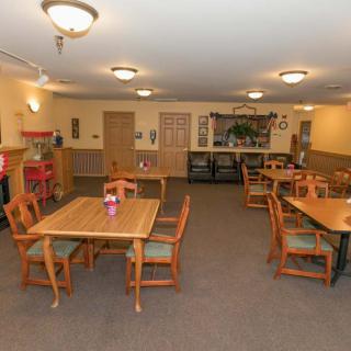 A cozy dining area with wooden tables and chairs, softly lit by ceiling lights.