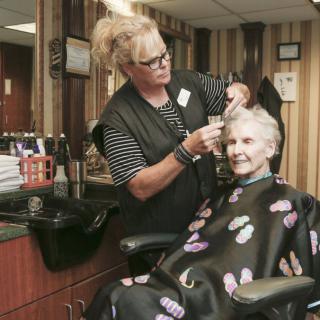 An elderly woman getting her hair styled by a hairdresser at a salon, both smiling.