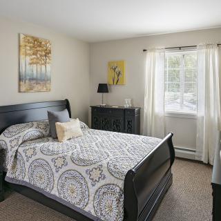 A cozy bedroom with a large bed, dresser, and window letting in natural light.