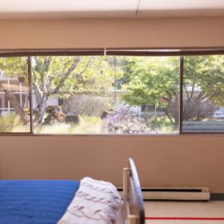 A cozy bedroom with a large window overlooking trees and greenery.