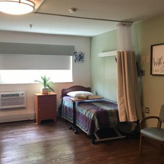 A well-lit hospital room featuring a bed, chair, and air conditioning unit.