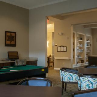 A cozy interior room with a pool table, tables and chairs, and bookshelves in the background.