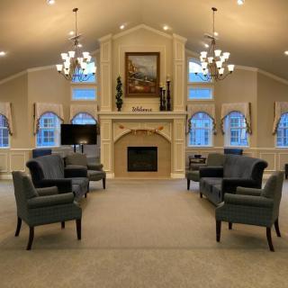 A spacious and elegant living room with a symmetrical arrangement of armchairs, featuring a central fireplace and large arched windows.