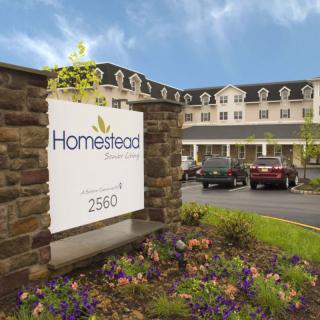 Exterior view of Homestead Suites, featuring a sign and landscaped entrance.