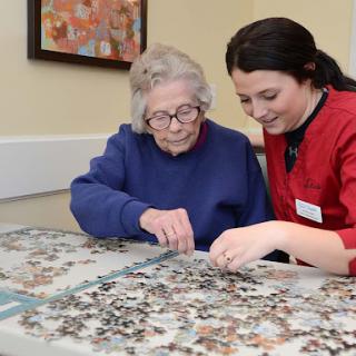 A caregiver and an elderly woman enjoy a puzzle together, fostering connection and engagement.