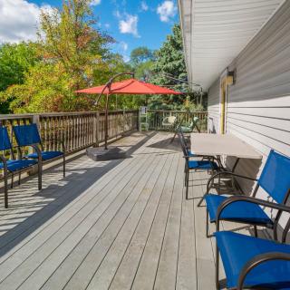 A sunny outdoor deck with blue chairs and a table under a red umbrella.