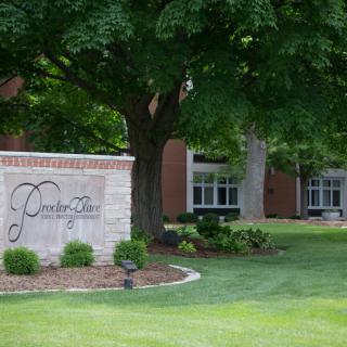 A scenic view of a college campus entrance with a welcoming sign and lush greenery.