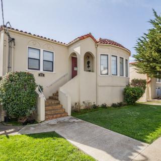 A quaint stucco house with a manicured front yard and steps leading to the entrance.