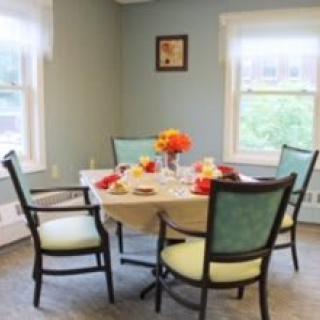 A cozy dining room with a round table, set with colorful flowers and place settings.