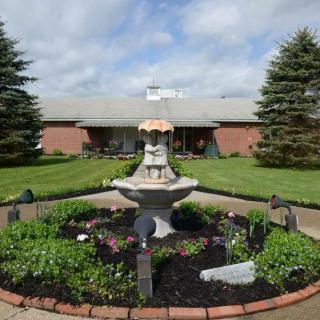 A beautifully landscaped garden with a central fountain, surrounded by greenery and a residential building in the background.