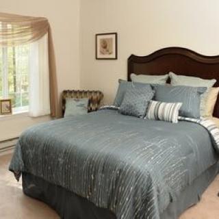 A cozy bedroom with a neatly made bed featuring blue bedding and several pillows, complemented by a large window allowing natural light to fill the space.