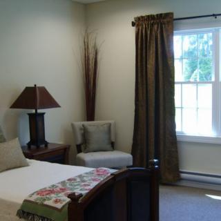A cozy bedroom with a bed, chair, lamp, and window with curtains.