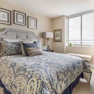 A well-decorated bedroom featuring a patterned bedspread, artwork on the walls, and natural light from a large window.