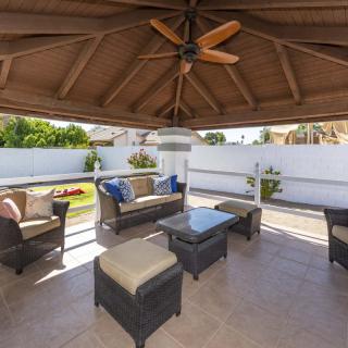 A cozy outdoor patio area with a gazebo, featuring wicker furniture and a ceiling fan, perfect for relaxation in a garden setting.