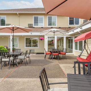 A well-furnished outdoor patio area with tables, chairs, and umbrellas, adjacent to a residential building.