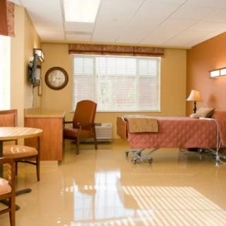 A clean and well-lit hospital room with a bed, table, chairs, and a window.