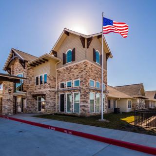 A stone-facade building with an American flag flying outside on a sunny day.