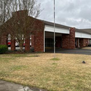A brick building with an entrance, surrounded by a lawn under a cloudy sky.