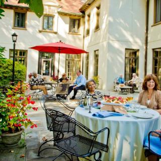 A group of people enjoying a meal on a sunny outdoor patio with a garden view.