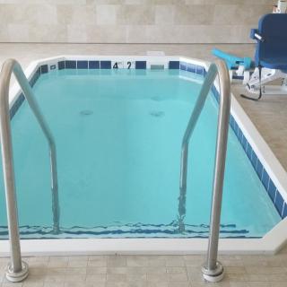 An indoor swimming pool with a metal ladder and an accessibility chair on the side.