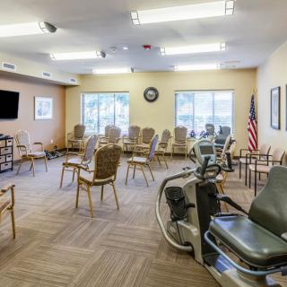 A well-lit waiting area with chairs arranged in a circle, featuring exercise equipment and a wall-mounted television.
