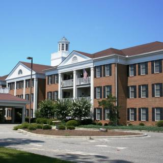 A colonial-style red brick building with a landscaped entrance and clear blue sky.
