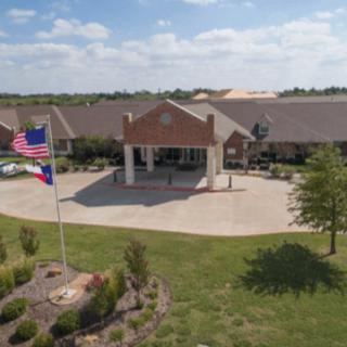 A large building with an entrance driveway, surrounded by greenery and featuring flags in the foreground.