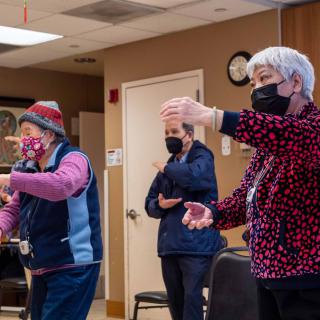 A group of seniors participating in an indoor exercise class while wearing masks.