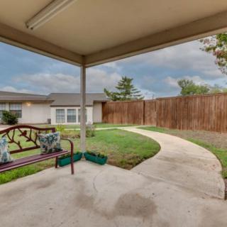 A cozy backyard with a covered patio, featuring outdoor seating and a well-maintained lawn enclosed by a wooden fence.