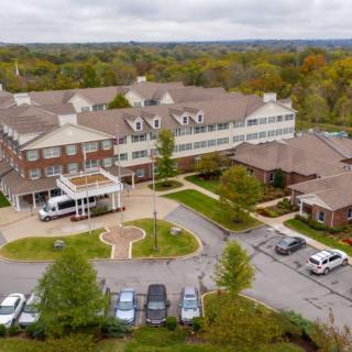 Aerial view of a large residential building surrounded by trees and a parking lot.