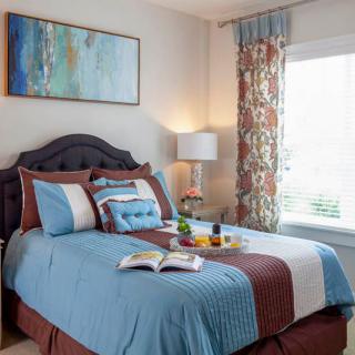 A cozy bedroom with a neatly made bed, colorful pillows, and a decorative painting on the wall.