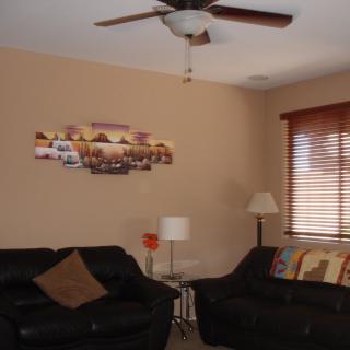 A cozy living room with two black sofas, a lamp, ceiling fan, and wall art.