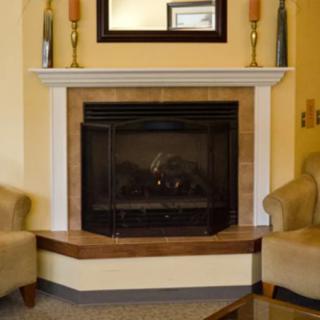 A cozy living room corner featuring a fireplace with a white mantel, flanked by two comfortable chairs and adorned with decorative items and a mirror above.