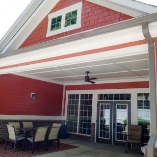 A cozy patio area with outdoor seating and a ceiling fan under a red gable roof.