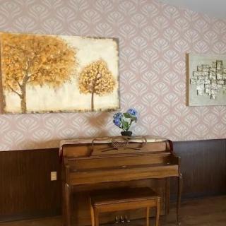 A cozy room featuring a wooden piano decorated with flowers, adorned by vintage wallpaper and artistic wall hangings.