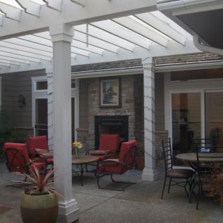 A cozy outdoor patio with red seating and a covered roof, featuring a fireplace and surrounding tables.
