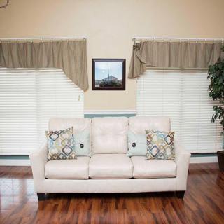 A cozy living room featuring a light-colored sofa with decorative pillows, wooden flooring, and elegant curtains.