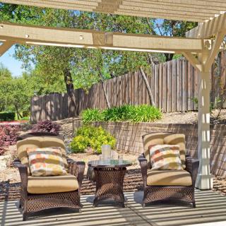A cozy patio area with wicker chairs under a pergola, surrounded by a lush garden.