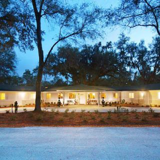 A modern, well-lit house surrounded by trees at dusk.