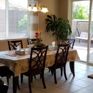 A sunlit dining room with a table set for a meal and large windows overlooking the outdoors.