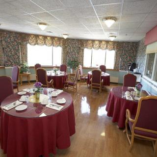 An elegant dining room with round tables covered in maroon tablecloths, set for a meal.
