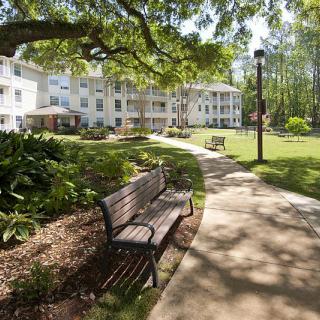 A peaceful park area with a bench, pathway, and a nearby building surrounded by trees and greenery.