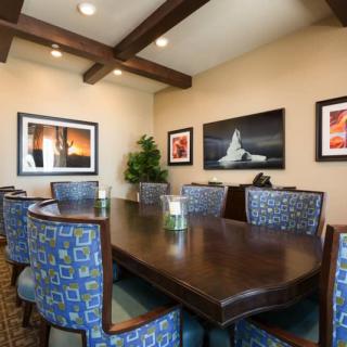 A modern conference room featuring a large wooden meeting table surrounded by upholstered chairs, with framed artwork on the walls and ceiling beams adding to the decor.