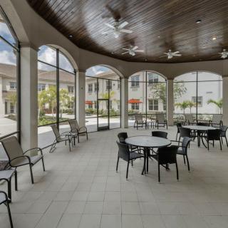 A spacious outdoor patio area with round tables and chairs, featuring large arched windows and ceiling fans.