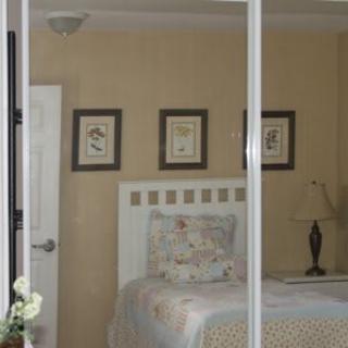 A cozy bedroom with a bed, decorative pillows, and wall art reflected in a mirror.