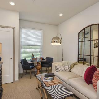 A cozy living room with a comfortable sofa, decorative pillows, and a small dining area by the window.