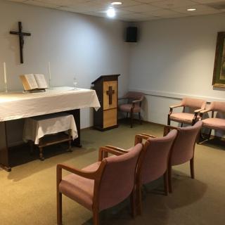 A small chapel interior with an altar, cross, and seating.