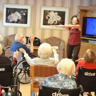 An activity leader guides a group of elderly individuals in an exercise session at a nursing home.