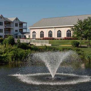 A scenic view of a pond with a fountain in front of elegant buildings.